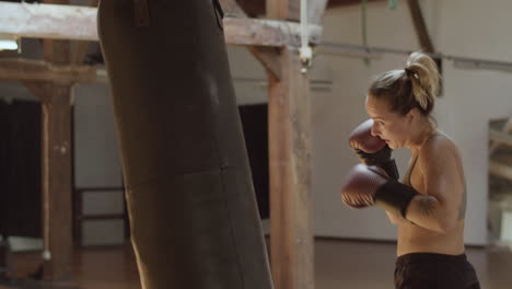 Medium-shot-of-tired-female-boxer-training-with-punching-bag